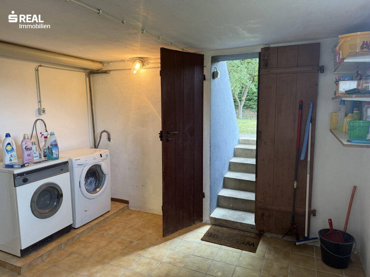 Praktischer Waschraum im Keller mit Waschmaschine, Trockner und Zugang zum Garten.