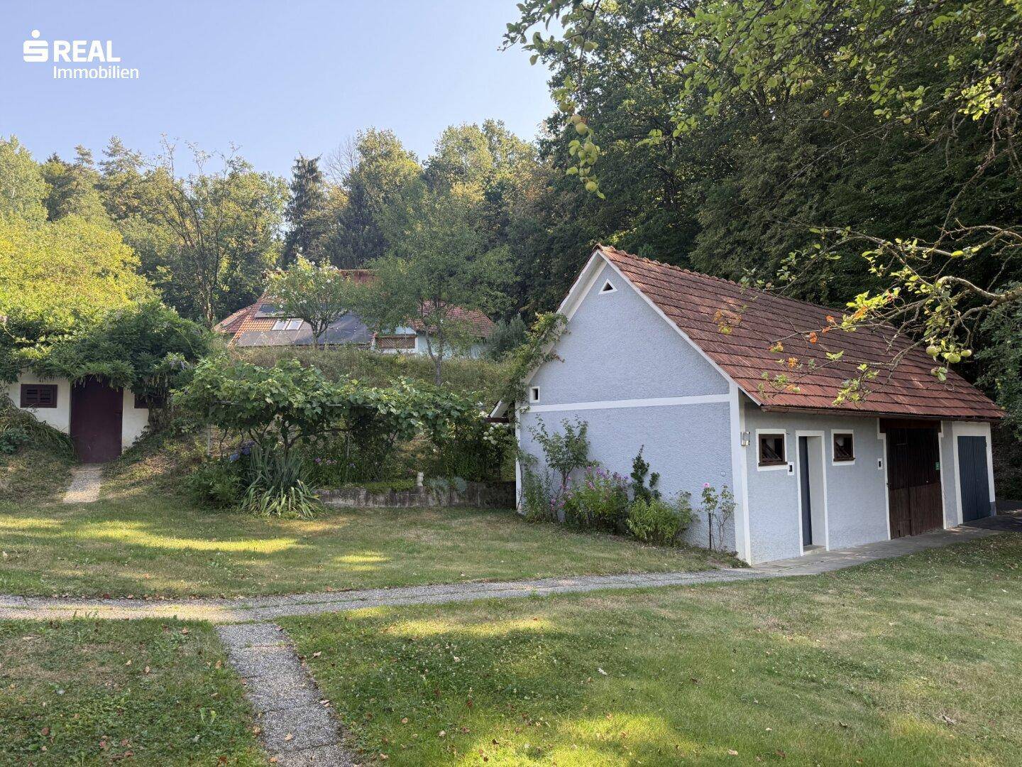 Mehrere Nebengebäude und ein gepflegter Gartenbereich mit Wegen und Bäumen.