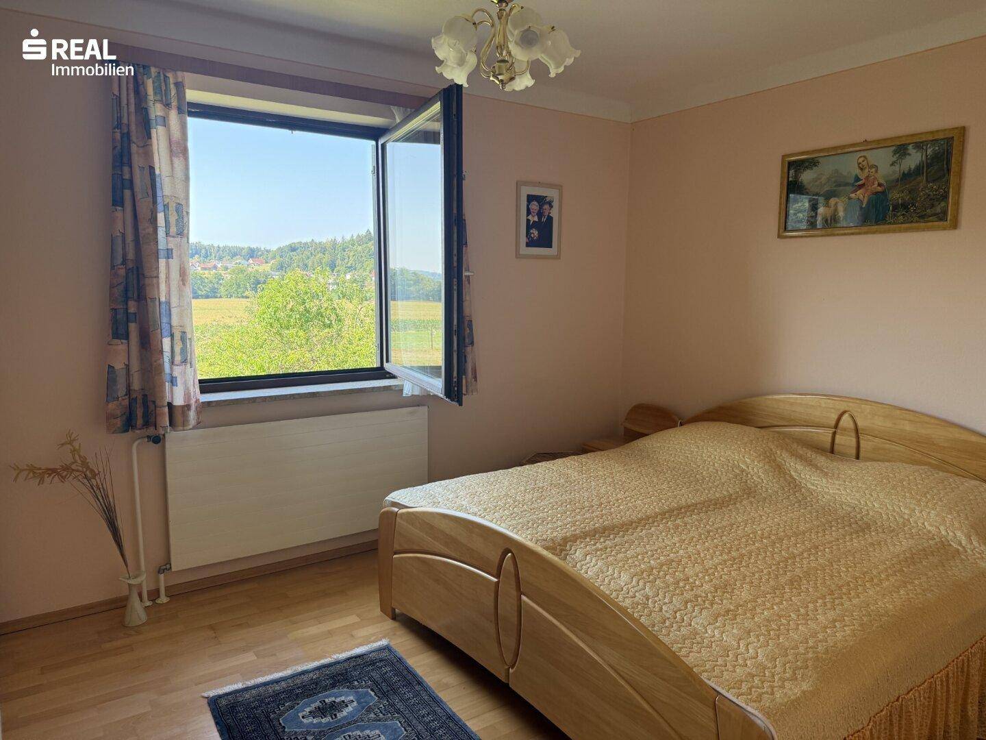 Helles Schlafzimmer mit Doppelbett und weitem Blick über die grüne Landschaft.