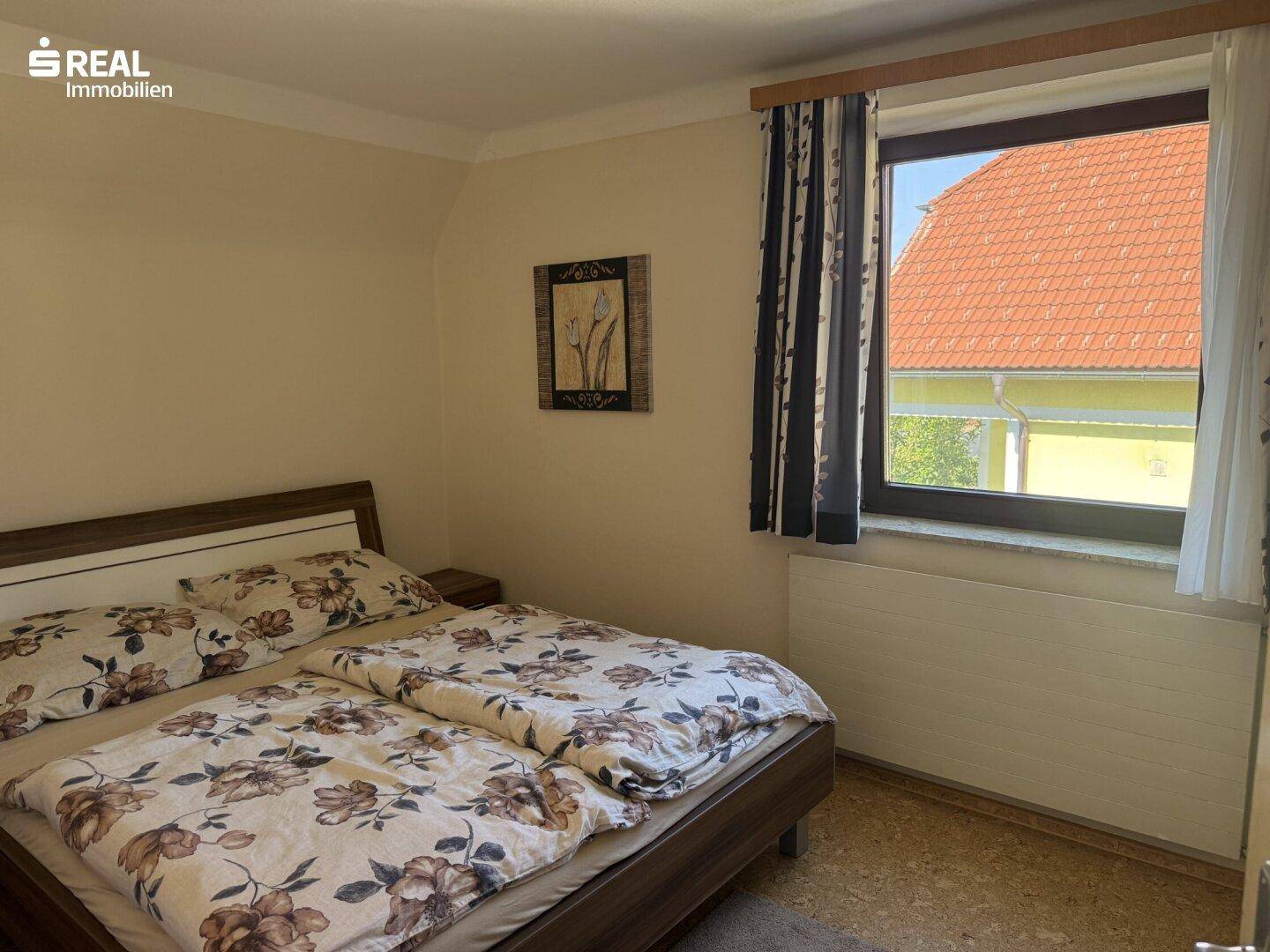 Schlafzimmer mit Doppelbett und Fenster, das einen Blick auf das Nachbardach bietet.