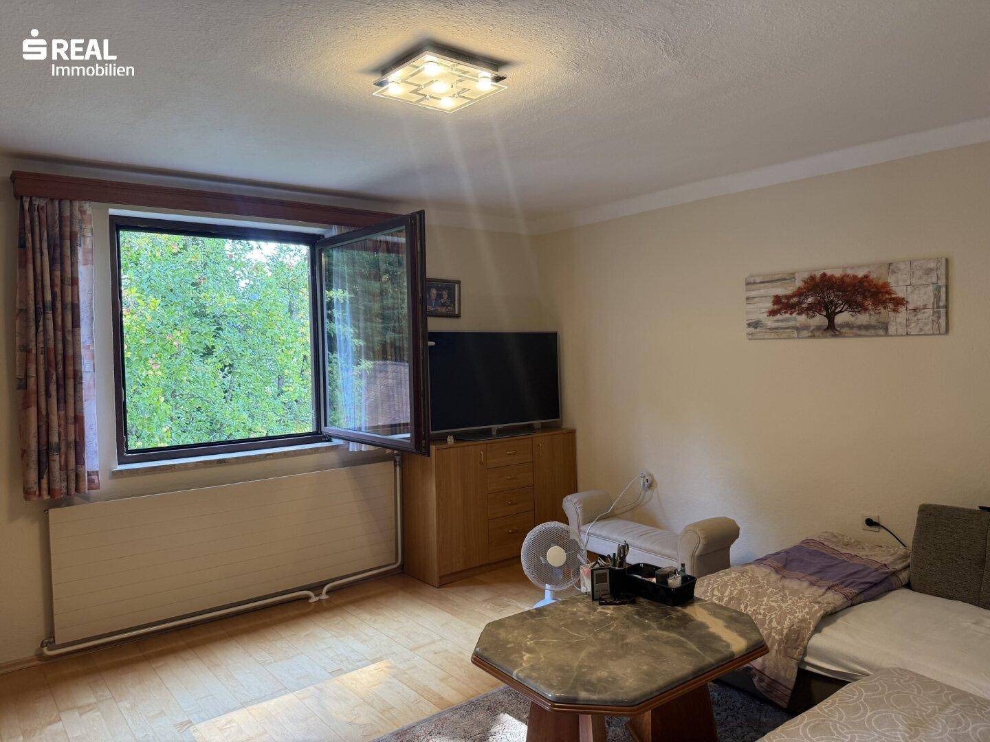 Helles Schlafzimmer mit Fenster und Blick ins Grüne, ausgestattet mit einem Fernseher.