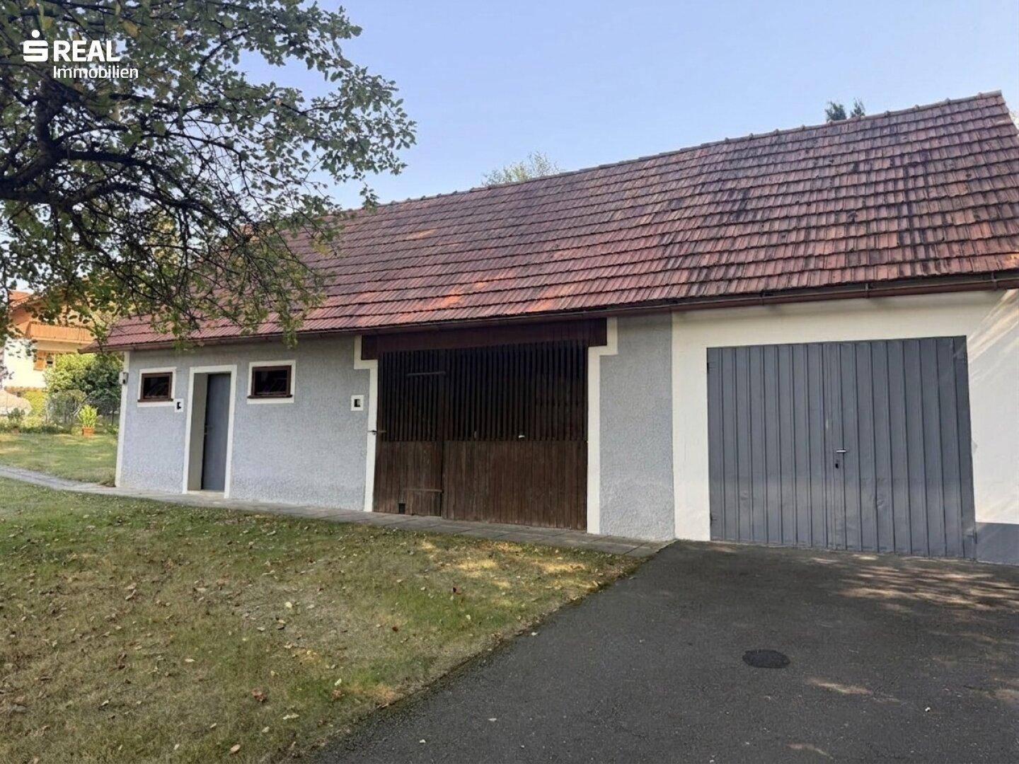 Großes Nebengebäude mit Garage und Scheunentor, ideal für Fahrzeuge oder Lagerung.