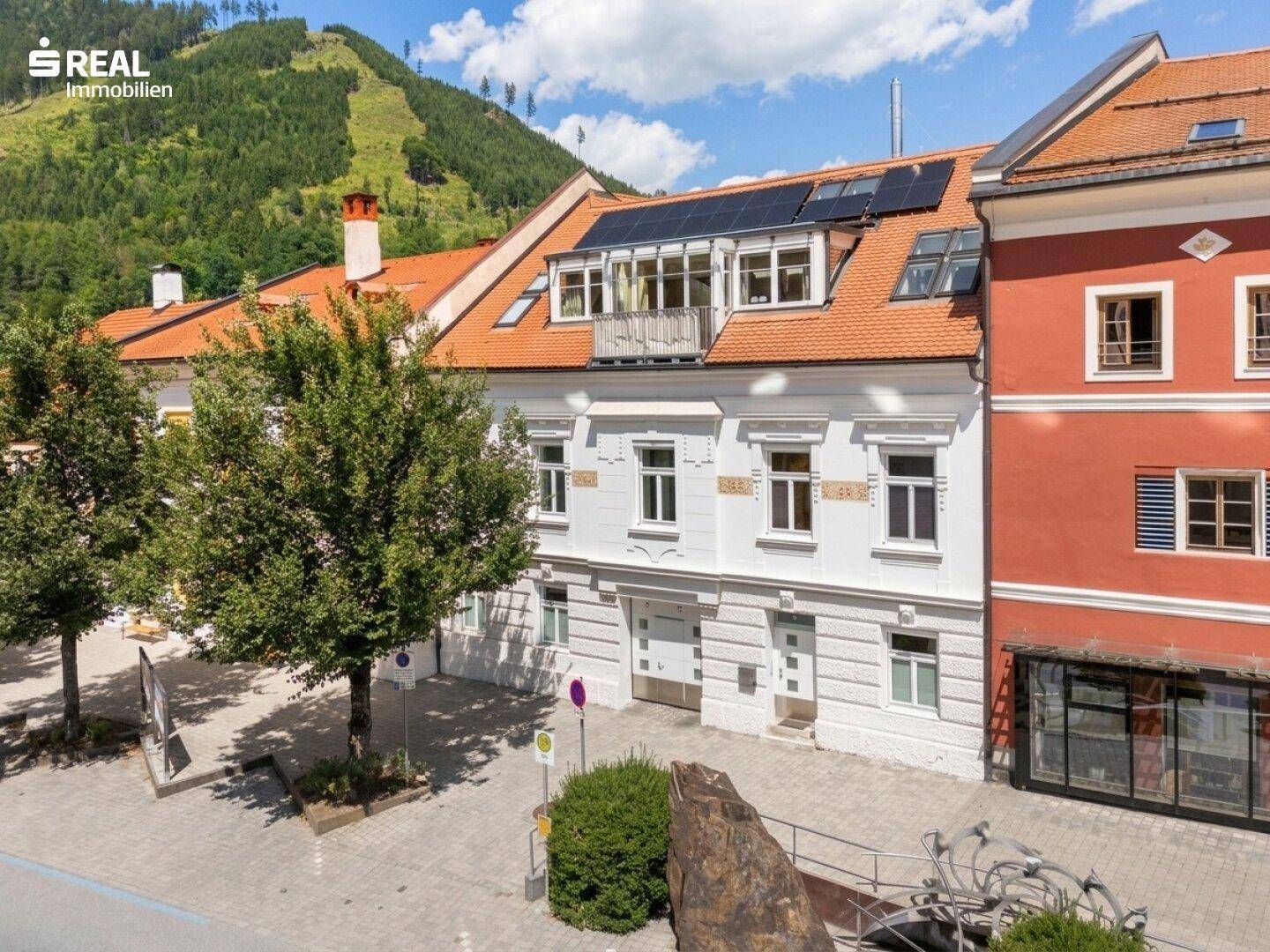 Historische Fassade des Gebäudes mit Solarpaneelen auf dem Dach und Blick auf die Berge.