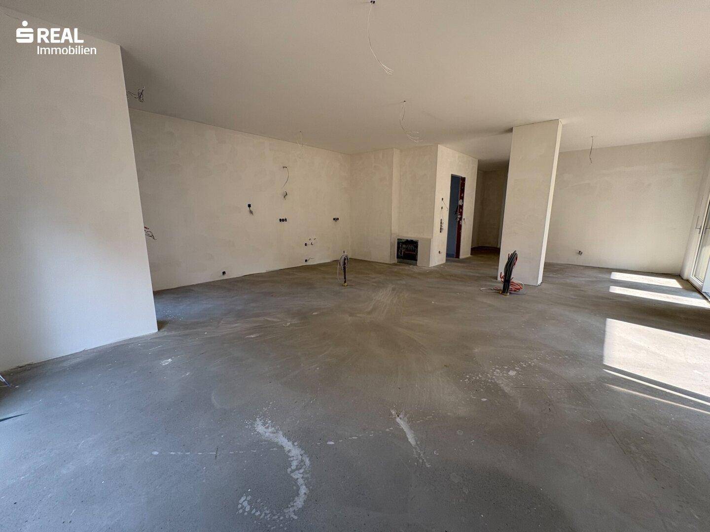 Weiterer Blick in den zukünftigen Wohnbereich im Rohbau mit Betonboden und vorbereiteten Elektroinstallationen.