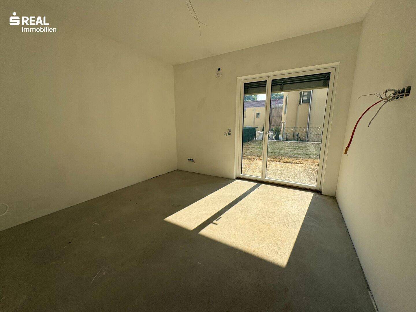 Weiterer Blick in den Rohbau eines Zimmers mit Schiebetür und viel natürlichem Licht, das den Raum erhellt.