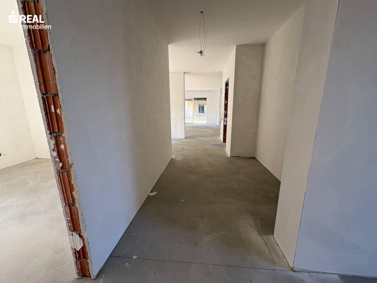 Langer Flur im Rohbau mit Betonboden, der zu den verschiedenen Räumen der Wohneinheit führt.