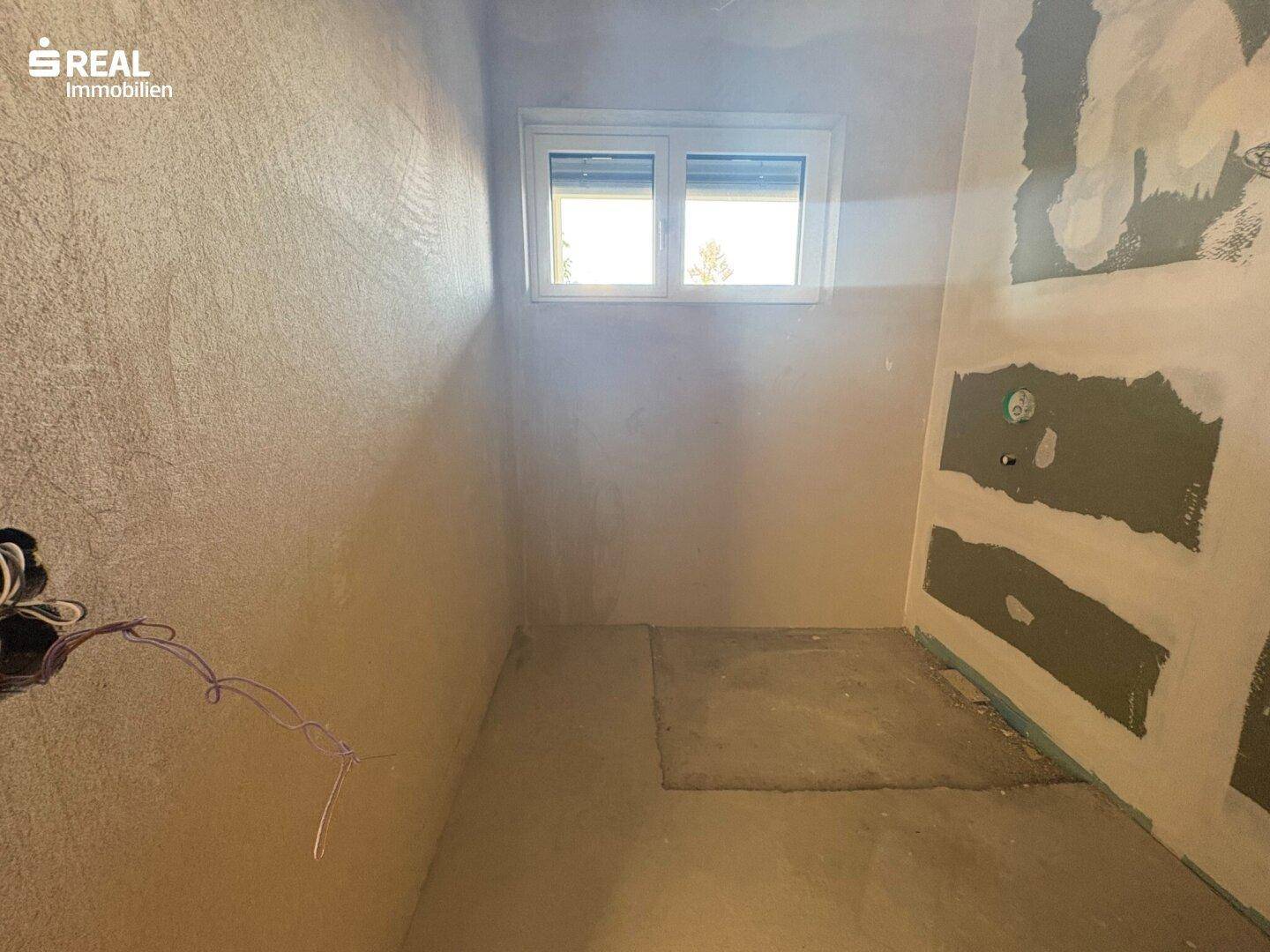 Raum im Rohbau mit Fenster, der als zukünftiges Badezimmer oder kleines Schlafzimmer dienen könnte.