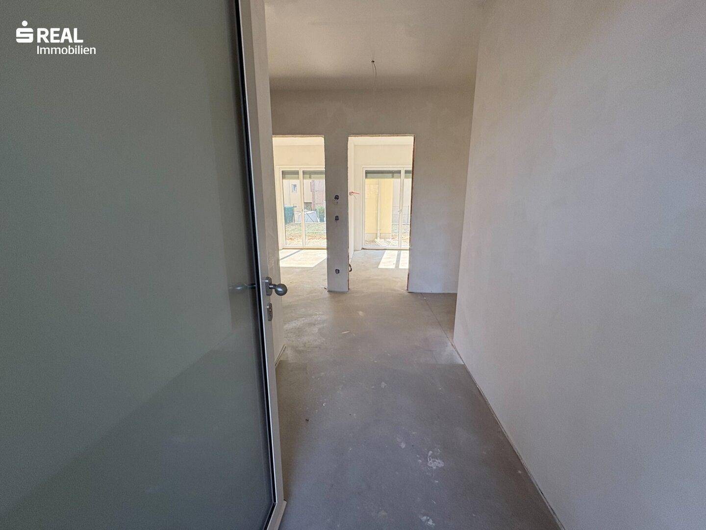 Flur im Rohbau mit Blick auf die Eingänge zu weiteren Räumen mit großen Schiebetüren.