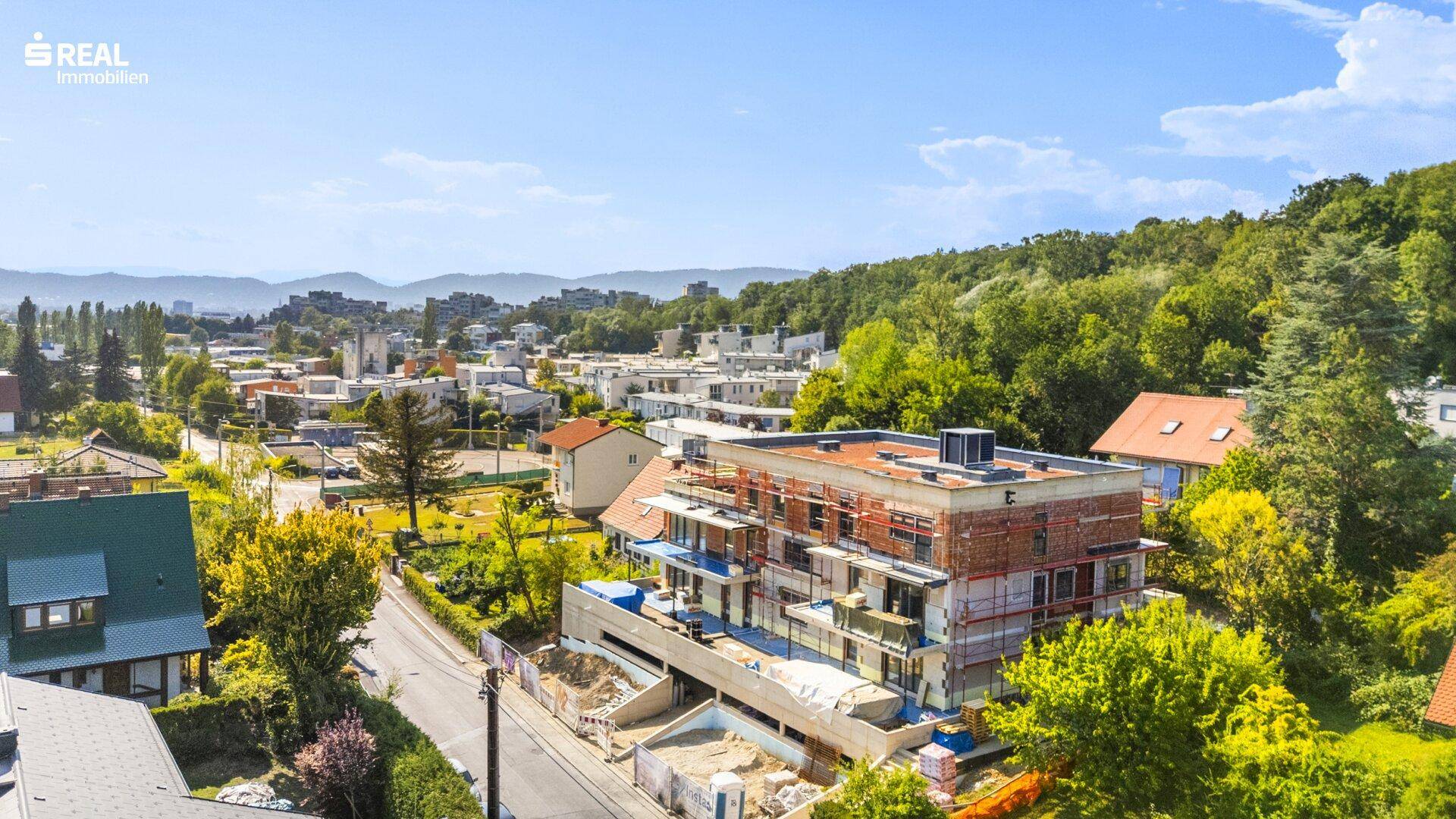 Weitläufige Luftaufnahme eines Neubauprojekts in einer grünen Wohngegend mit Fernblick.