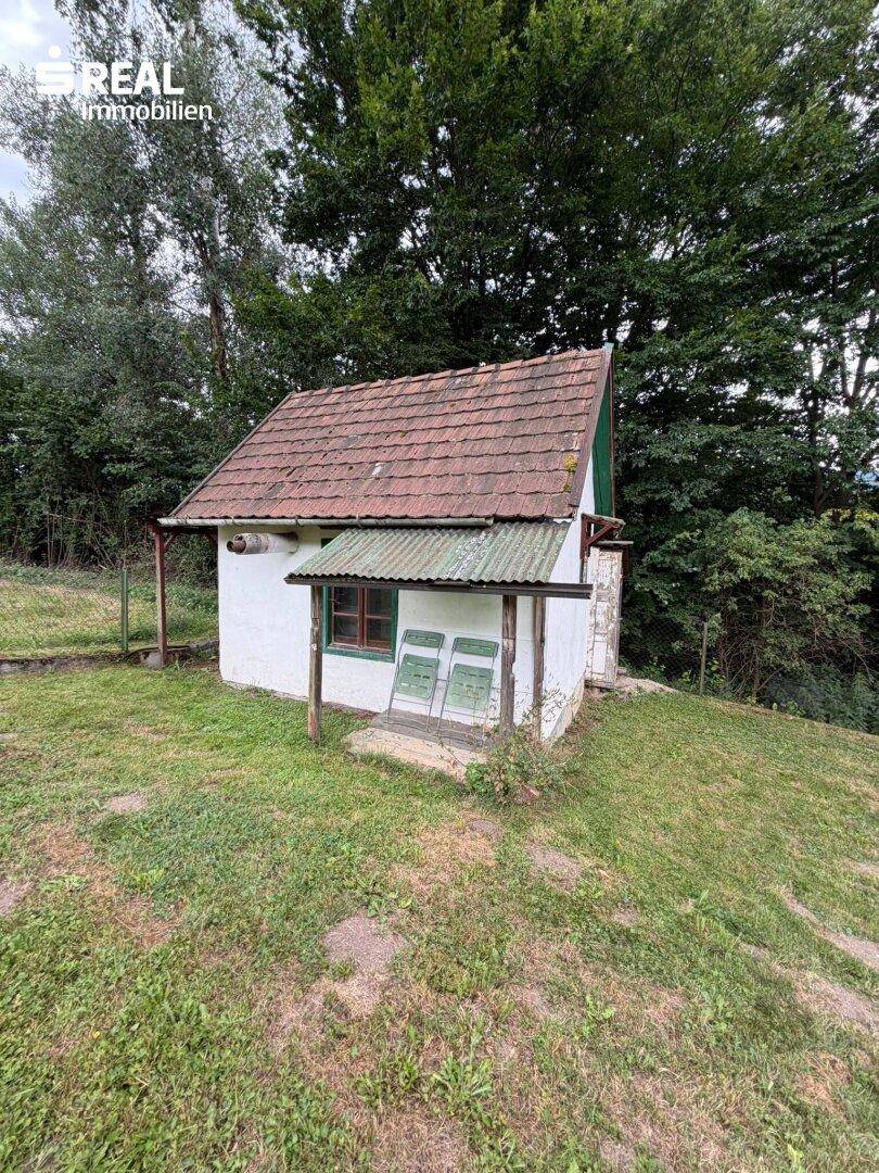 Rustikale kleine Hütte mit Vordach und einfacher Ausstattung, umgeben von Wiesen.