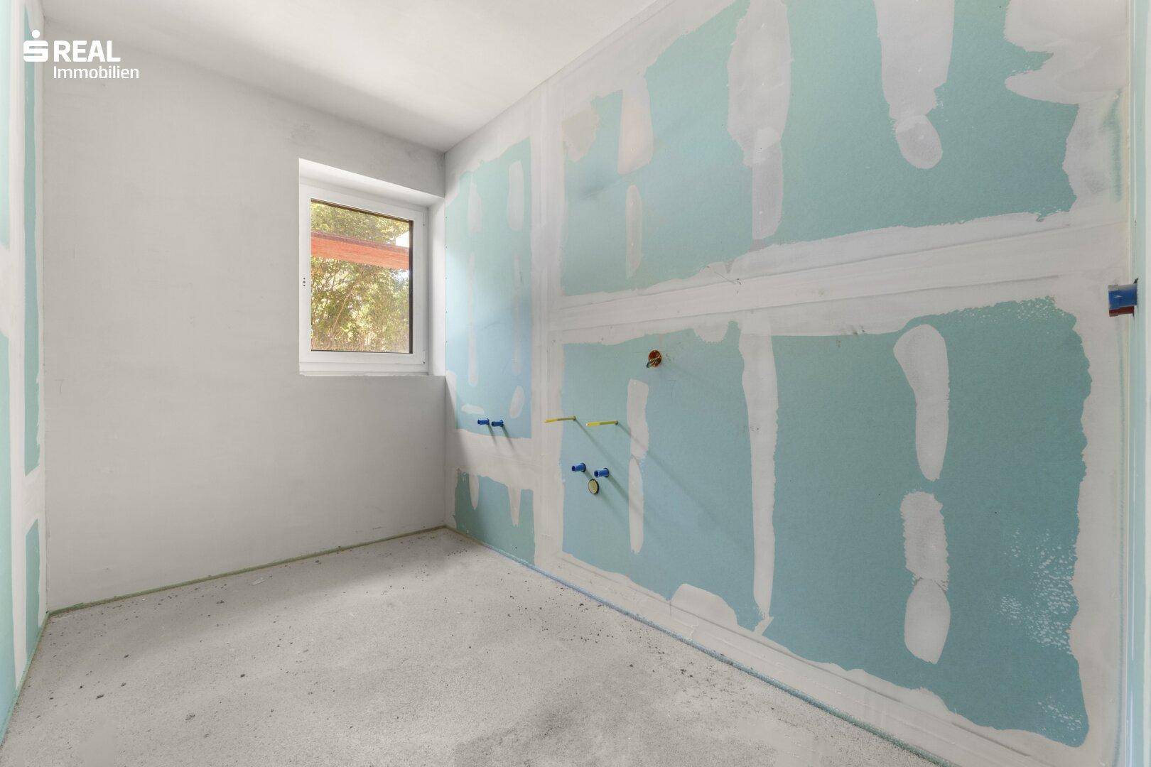 Rohbau eines Badezimmers mit blauen Trockenbauplatten, Betonboden und sichtbaren Wasseranschlüssen.