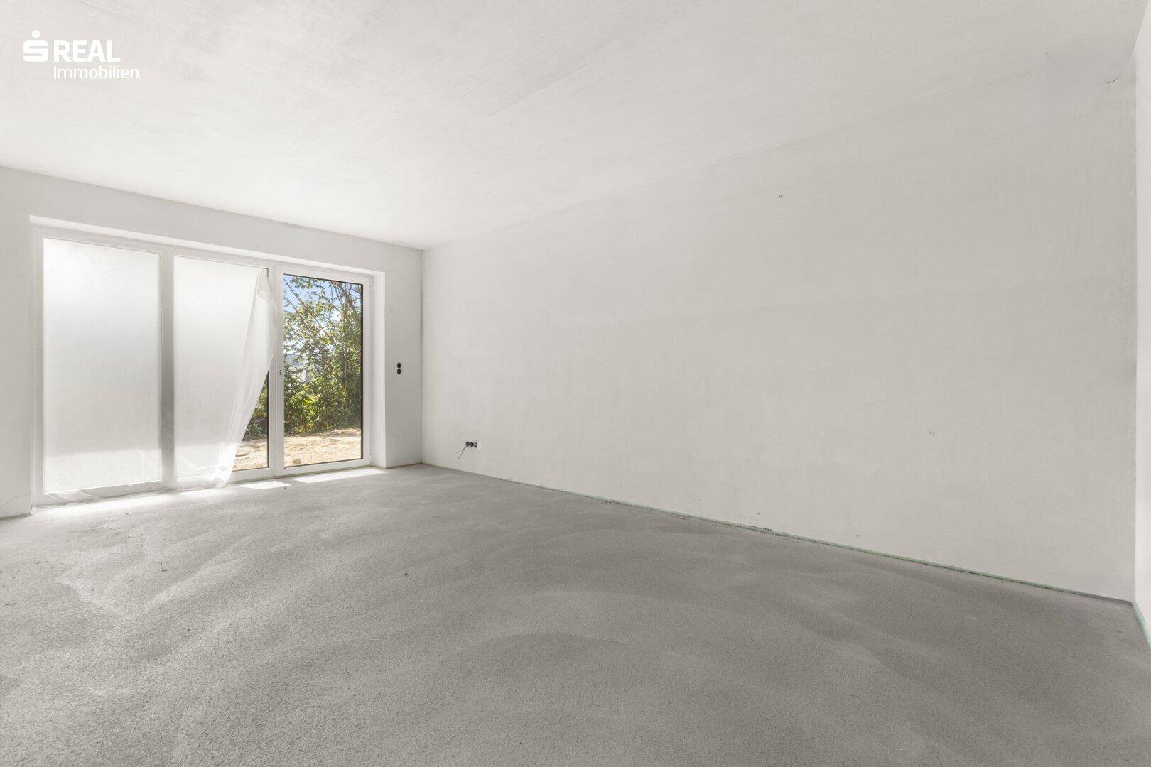 Heller Rohbau eines Raumes mit Betonboden und einer großen Glasschiebetür, die viel Licht spendet.