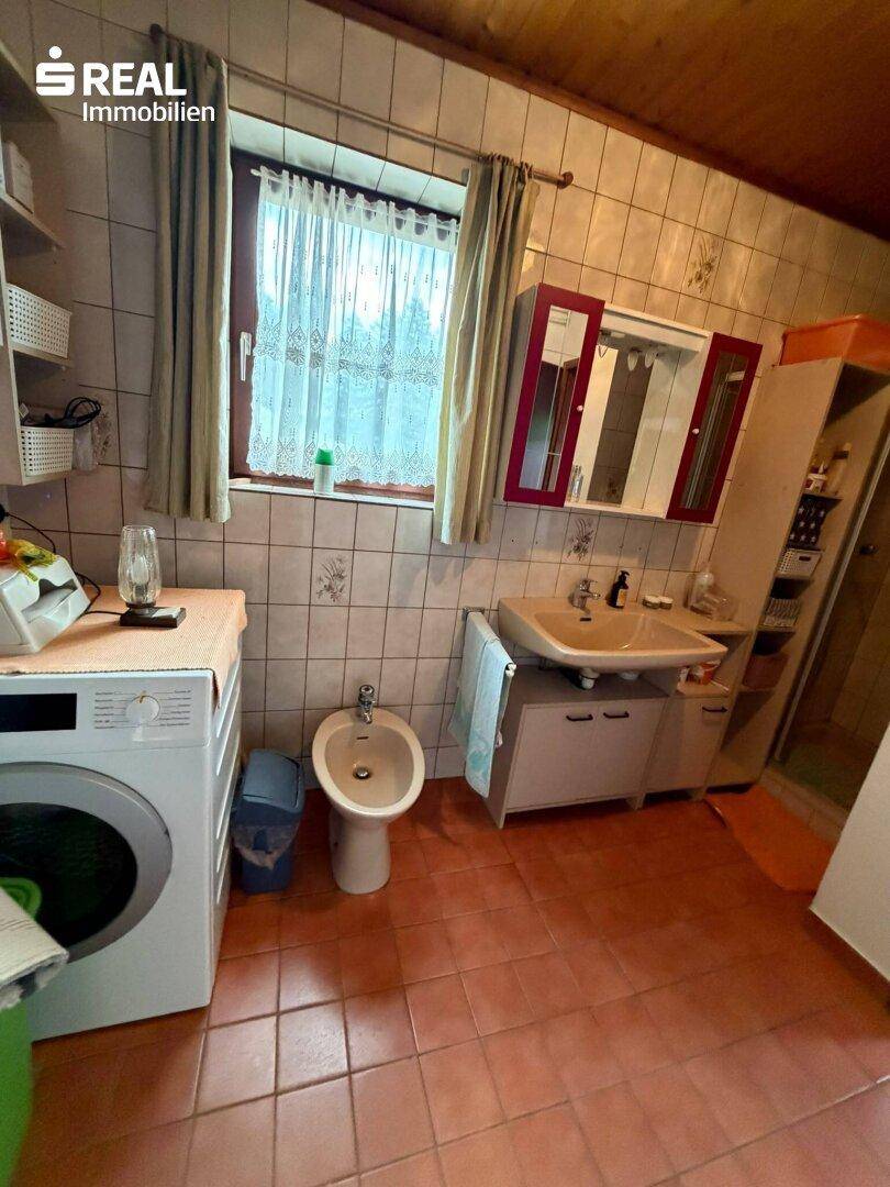 Badezimmer mit Terrakotta-Fliesen, Waschmaschine, Bidet und Holzdecke.