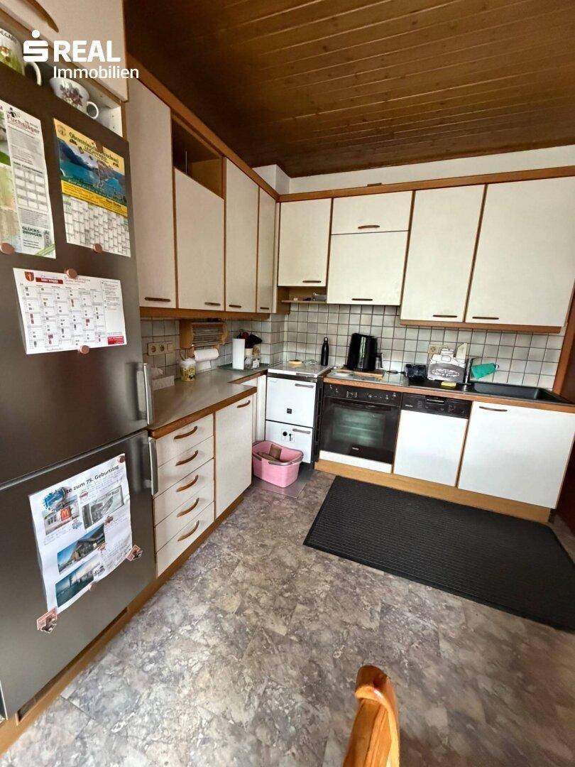 Funktionale Küche mit weißen Schränken, Kühlschrank und Spülmaschine, mit Holzdecke.