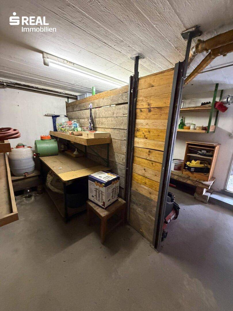 Rustikaler Kellerraum mit Holzverkleidung, Regalen und Stauraum für verschiedene Gegenstände.