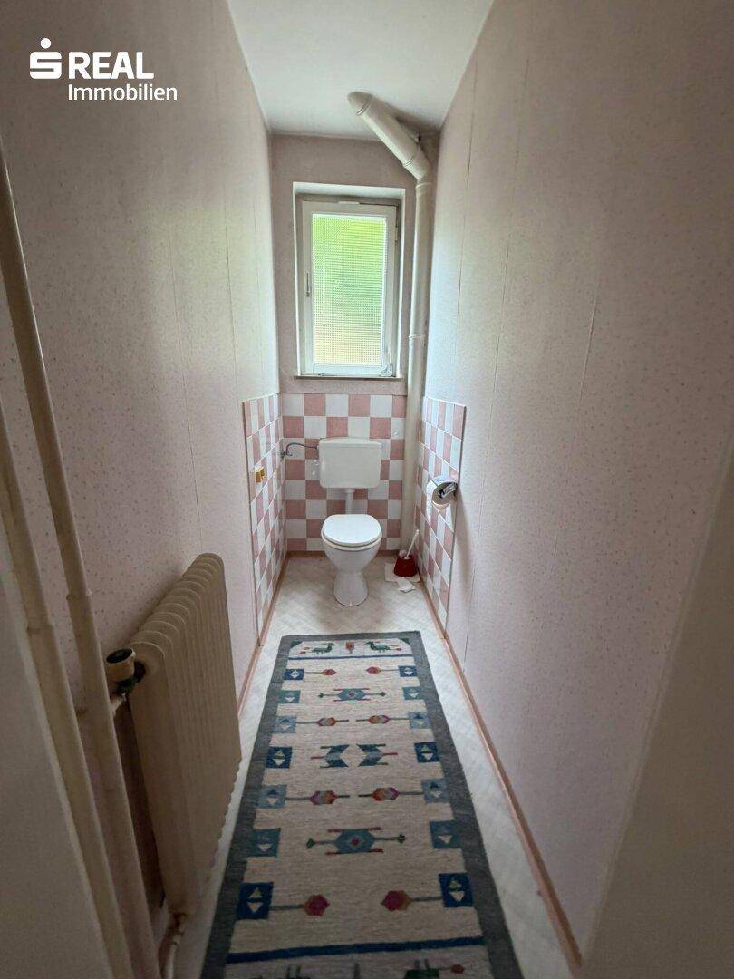 Schmale Gästetoilette mit Fenster, WC und rosa-weiß karierten Fliesen an der Wand.