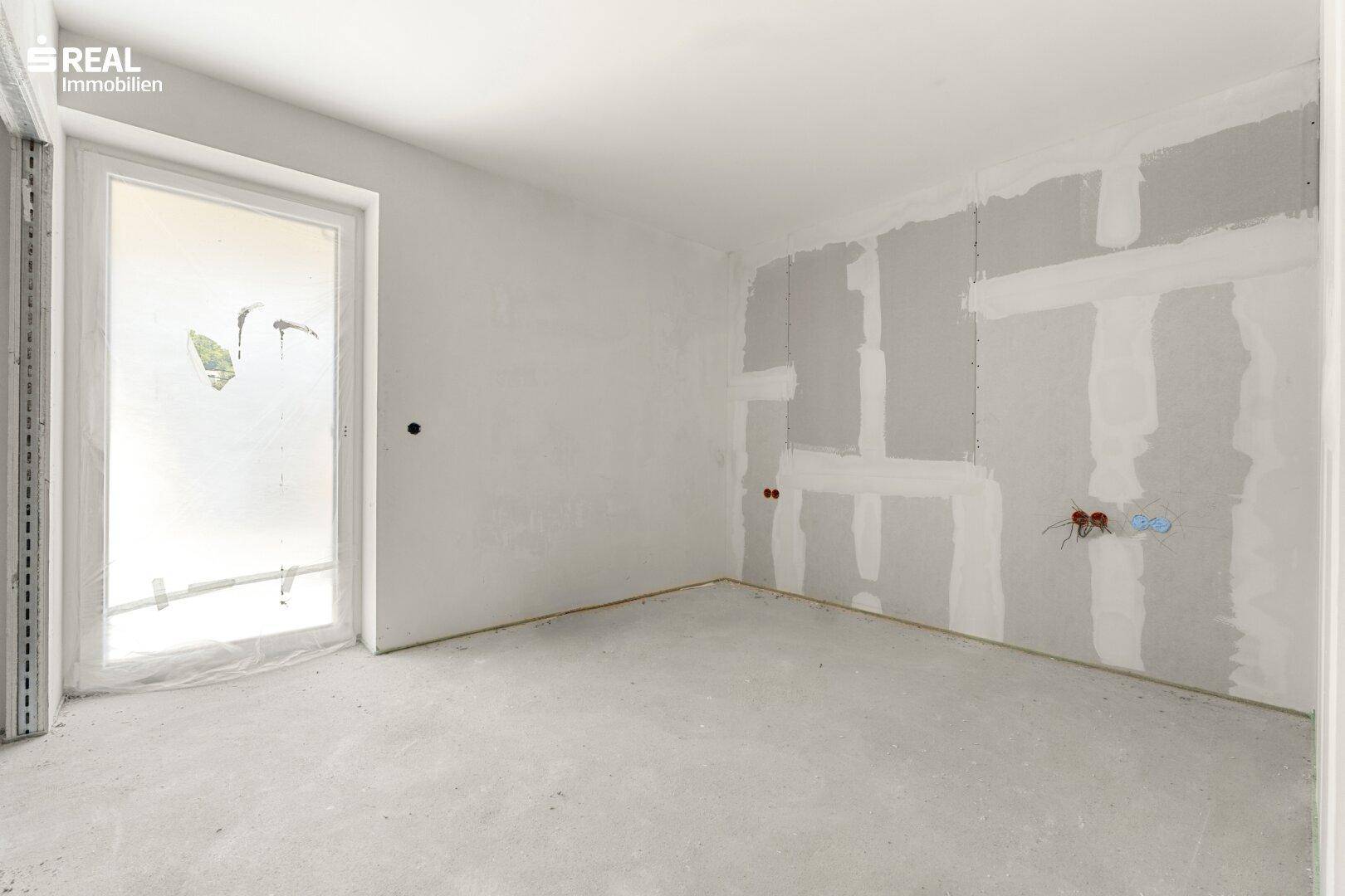 Heller Raum im Rohbau mit einer Tür zu einem möglichen Balkon oder Terrasse und Betonboden.