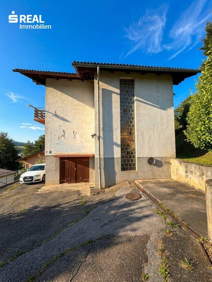 Seitenansicht des Hauses mit großer Glasbausteinwand und Zufahrt zum Untergeschoss.