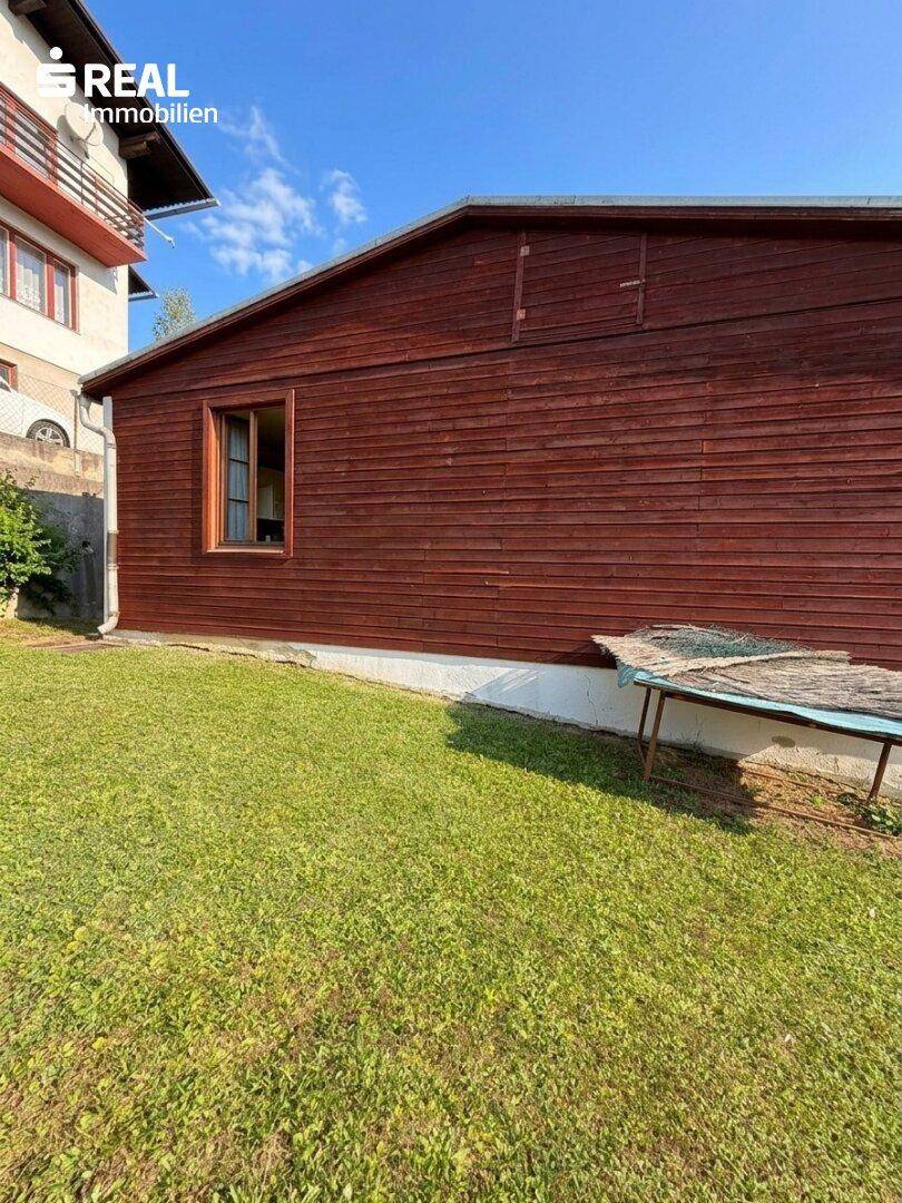 Seitenansicht eines Holzhauses mit Fenster und gepflegtem Rasen im Vordergrund.