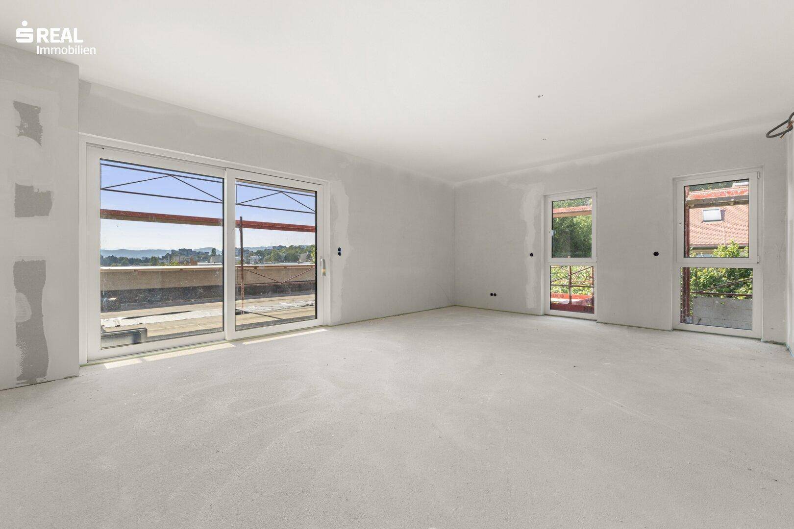 Geräumiger Wohnbereich im Rohbau mit großen Fenstern und Zugang zur zukünftigen Terrasse.