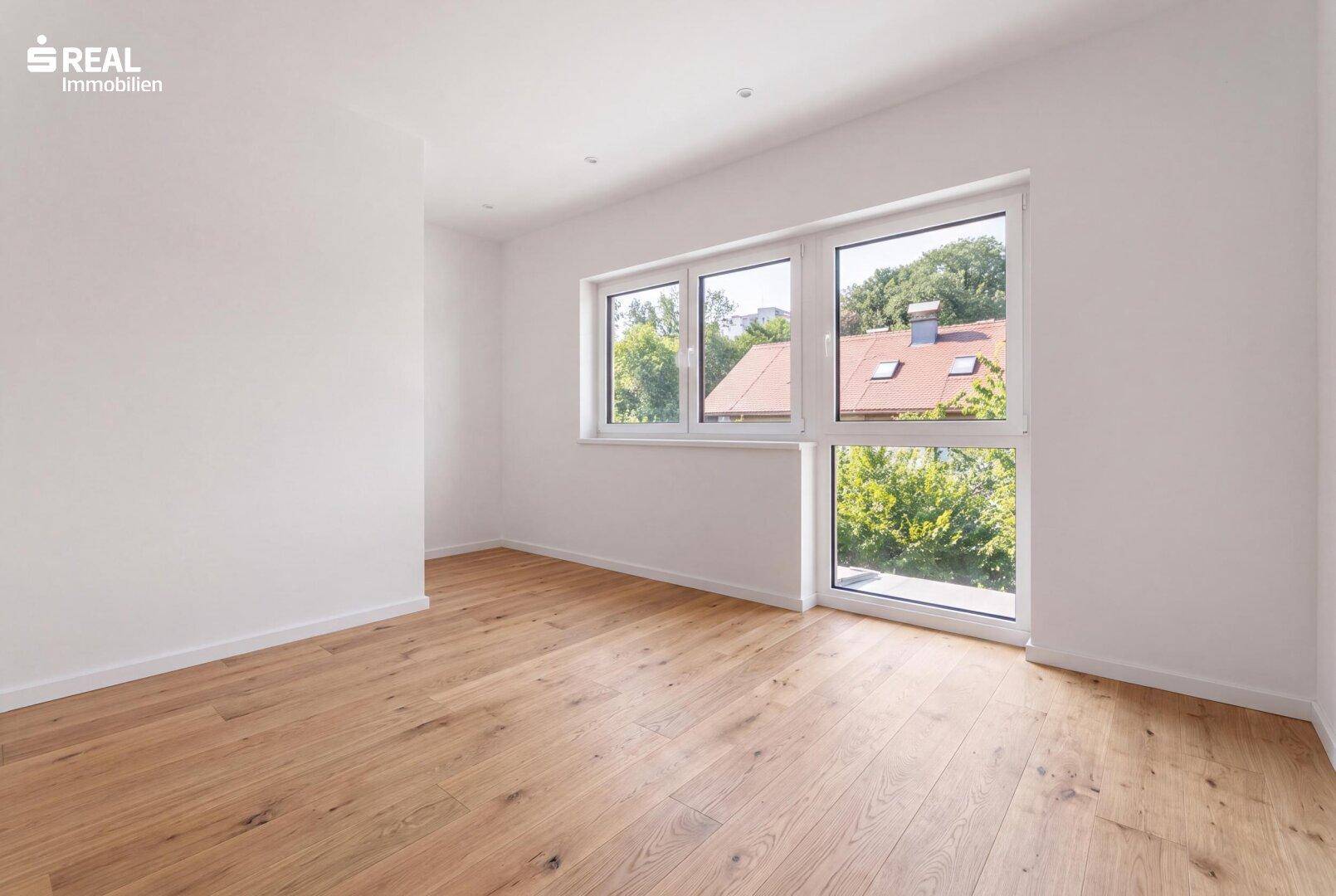 Helles Zimmer mit Holzboden und großen Fenstern, die viel Tageslicht hereinlassen.