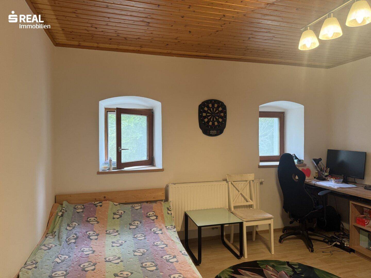 Schlafzimmer mit Holzbett, Schreibtisch und Holzdecke.