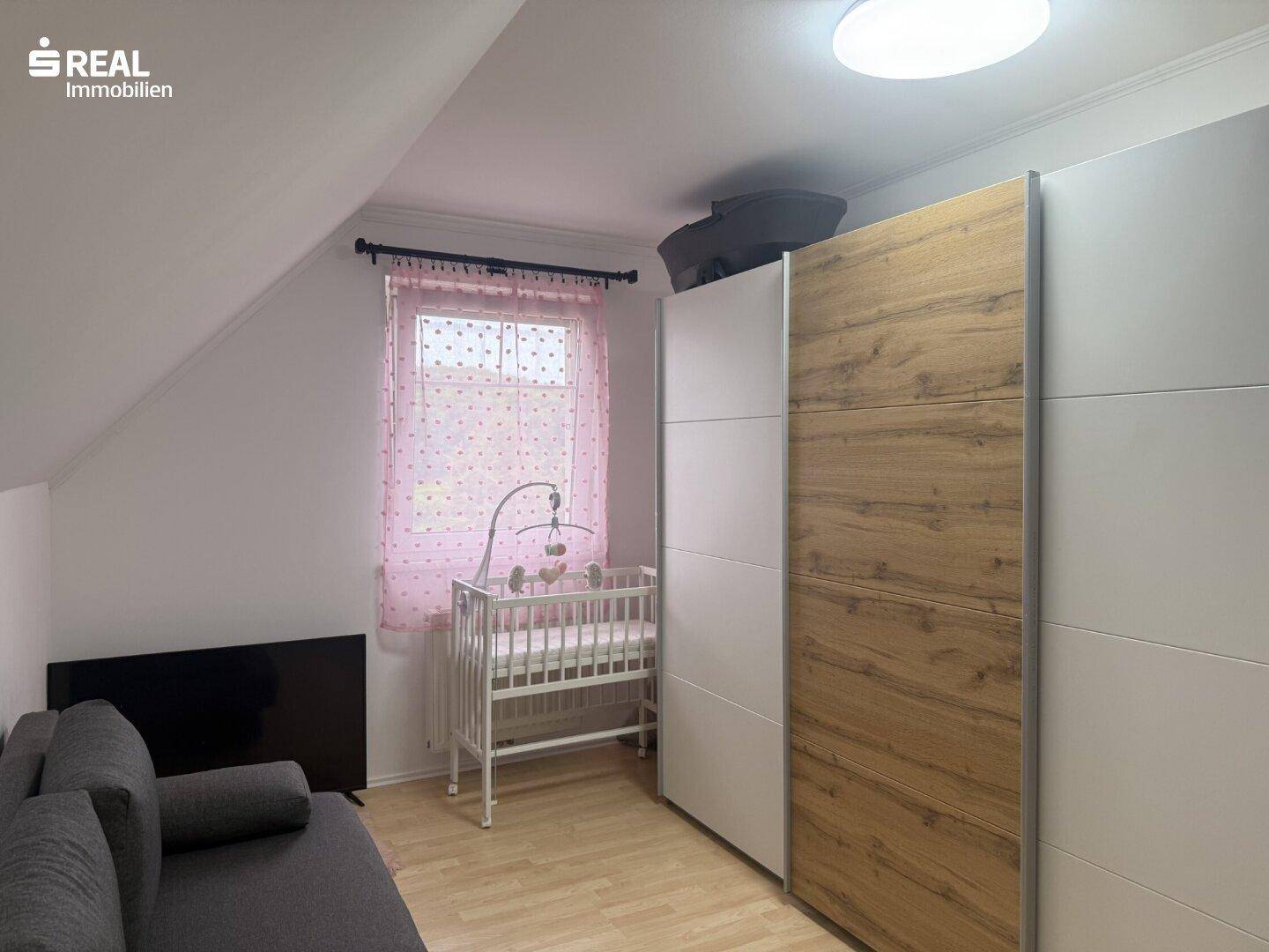 Kinderzimmer mit Dachschräge, Kleiderschrank und Babybett.