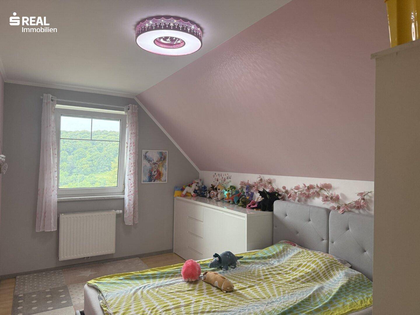Kinderzimmer mit rosa Wänden, Dachschräge und Blick auf die Landschaft.