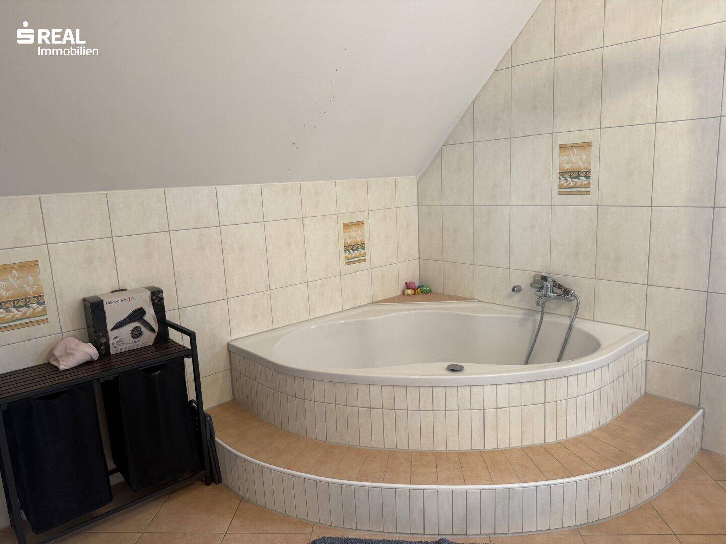 Badezimmer mit Eckbadewanne und Fliesen an Wänden und Boden.