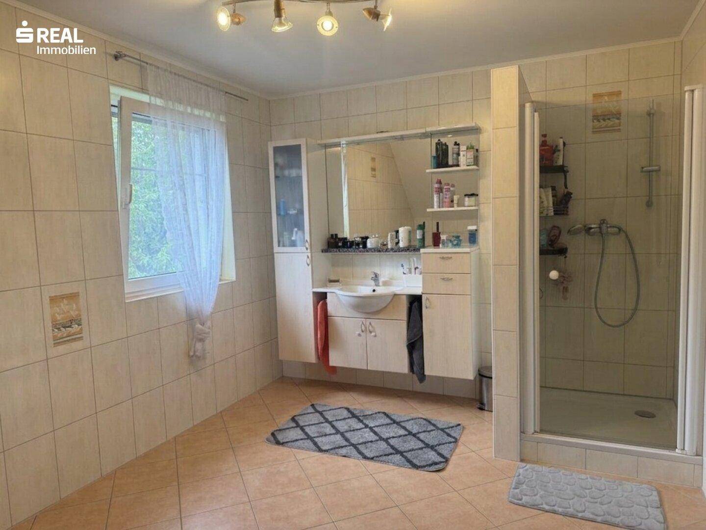 Geräumiges Badezimmer mit Dusche, Waschbecken und Fliesenboden.