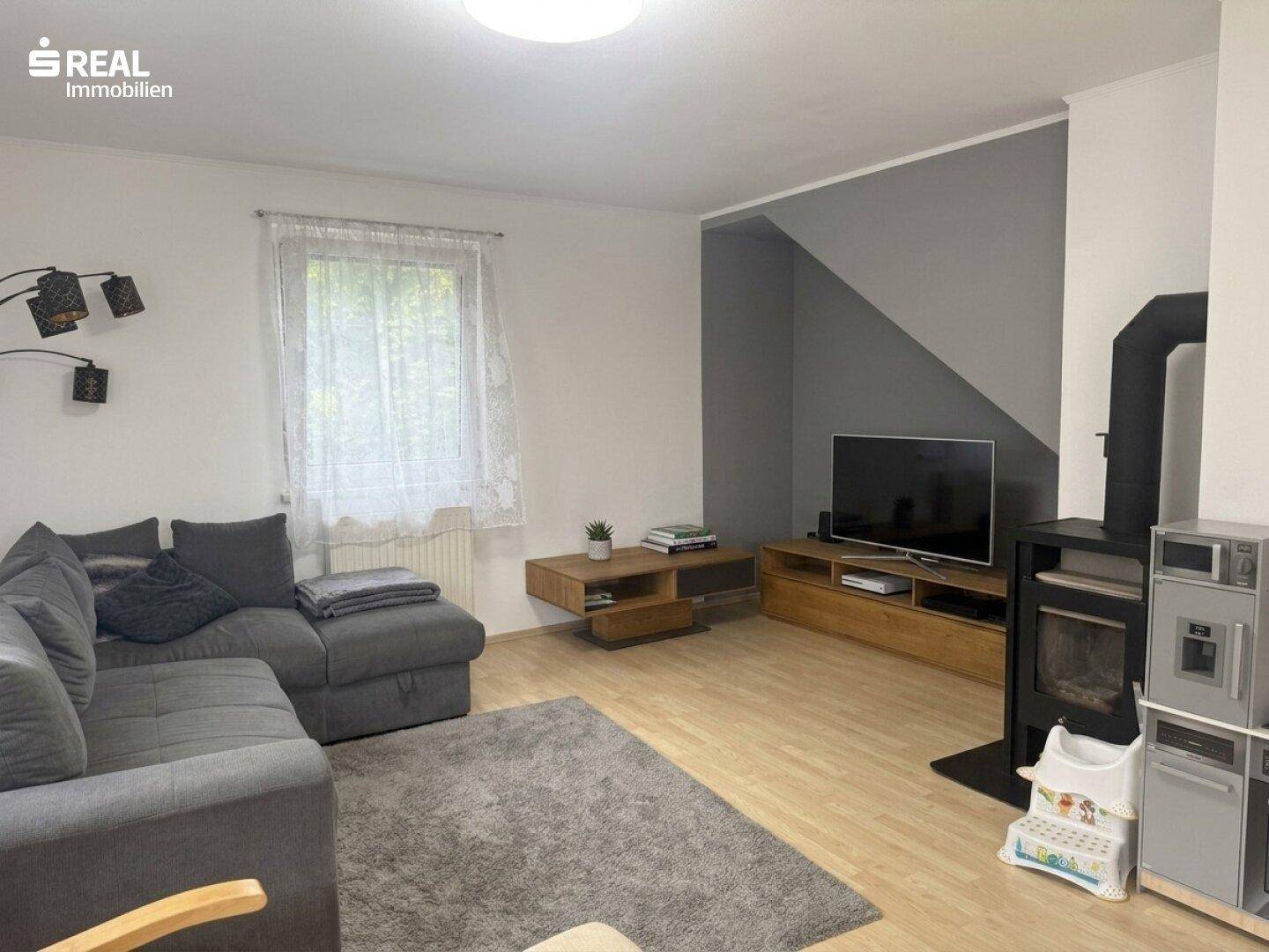 Wohnzimmer mit grauem Ecksofa, Holzofen und modernem TV-Möbel.