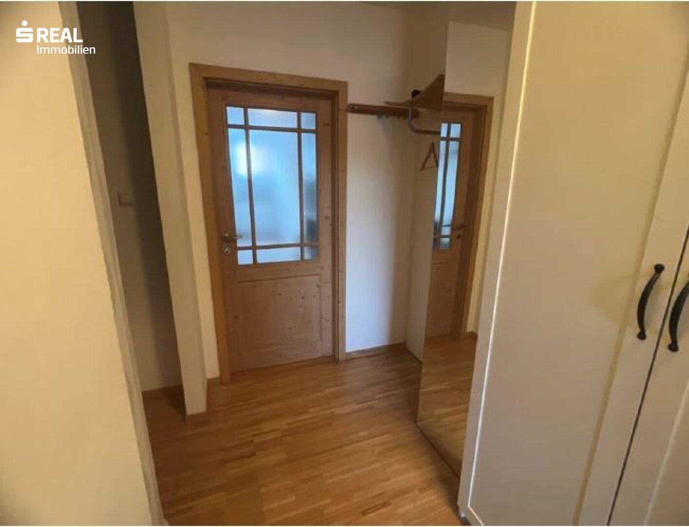 Heller Flur mit Holzboden, Spiegel und Holztüren, die zu weiteren Räumen führen.