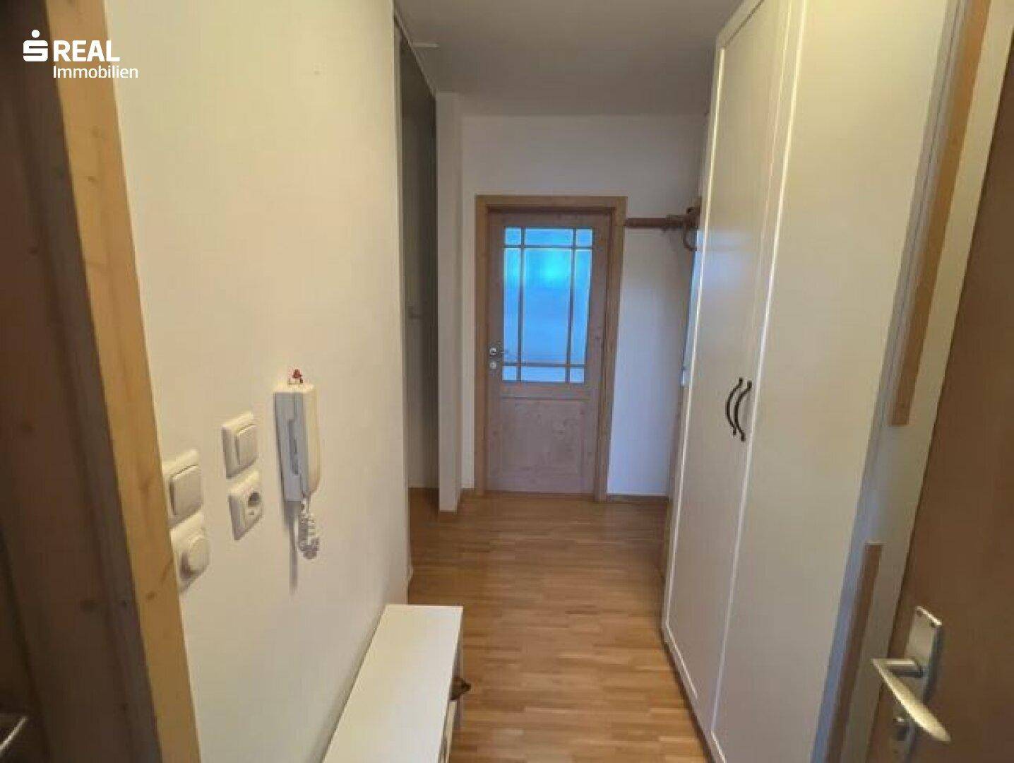 Eingangsbereich mit hellem Holzboden, weißem Schrank und einer Holztür mit Glaseinsatz.