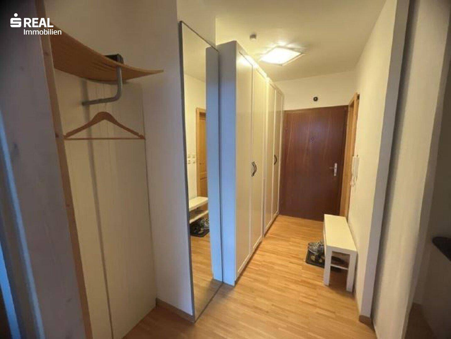 Geräumiger Flur mit Holzboden, großem Spiegel und weißen Einbauschränken für Stauraum.