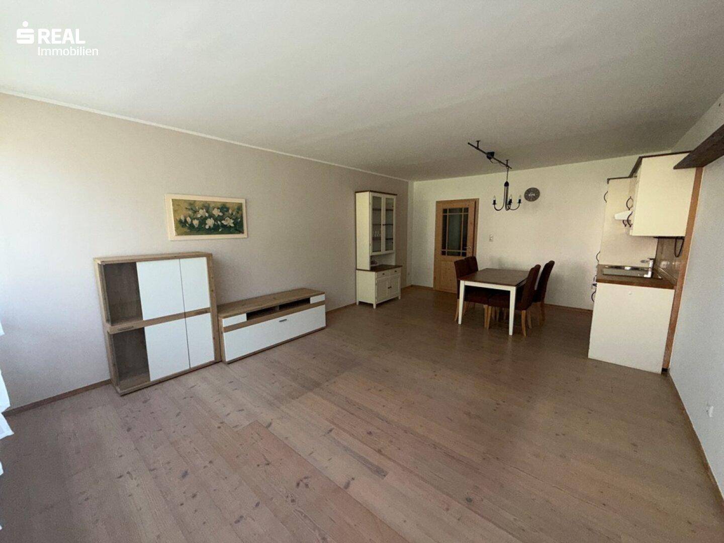 Heller Wohnbereich mit Holzboden, Esstisch und Schränken, offen zur Küche.