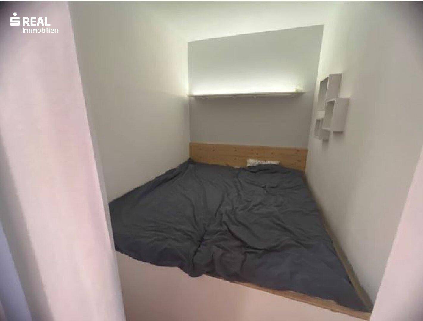 Kleiner, gemütlicher Schlafbereich mit Holzbettrahmen und indirekter Beleuchtung.