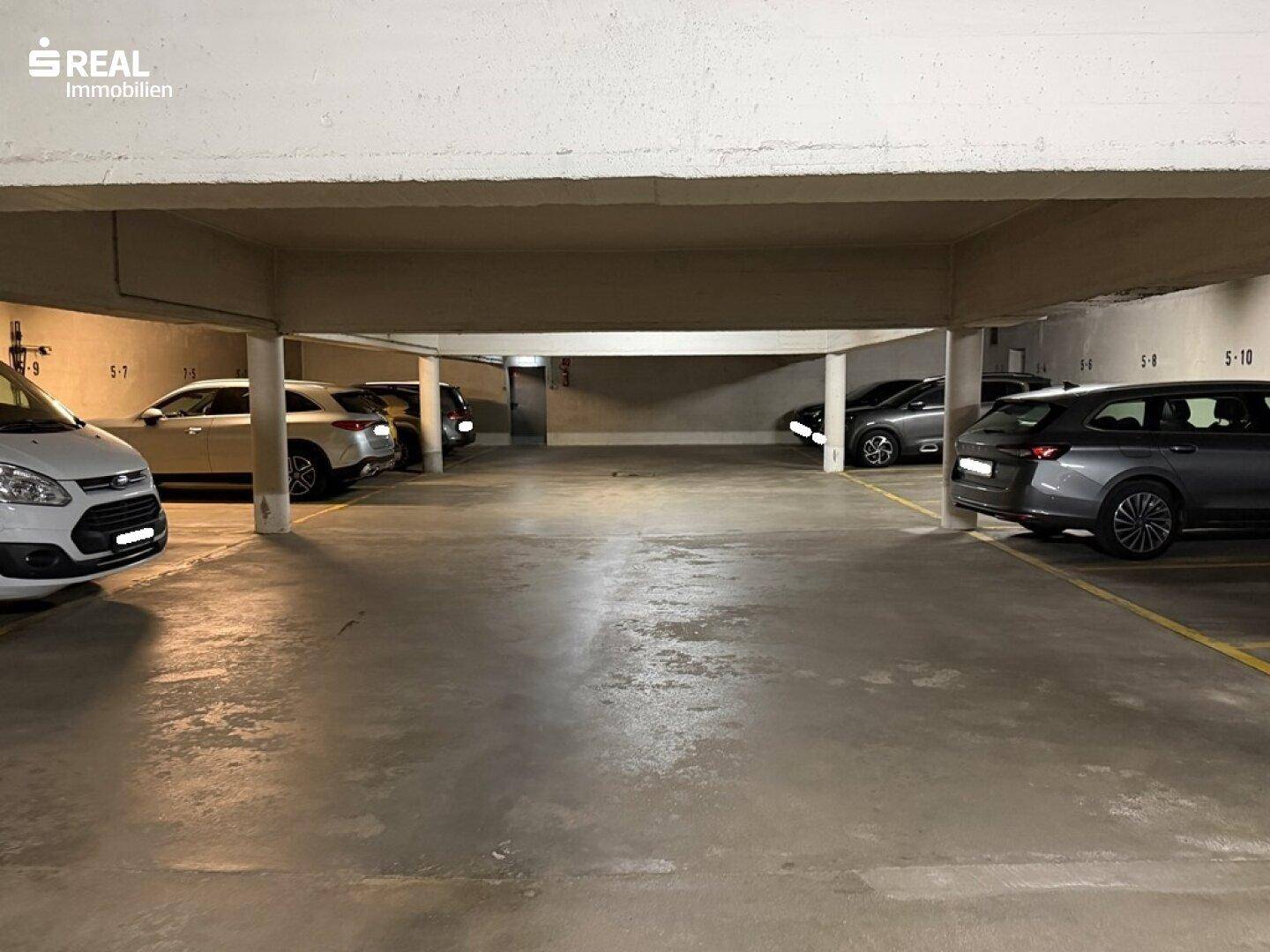 Geräumige Tiefgarage mit mehreren geparkten Autos und Betonstützen.