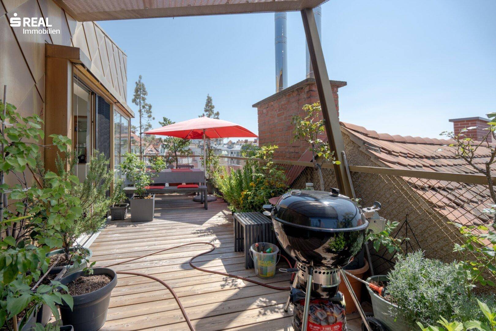 Geräumige Dachterrasse mit Holzdeck, Grillbereich und Pflanzen in Töpfen.
