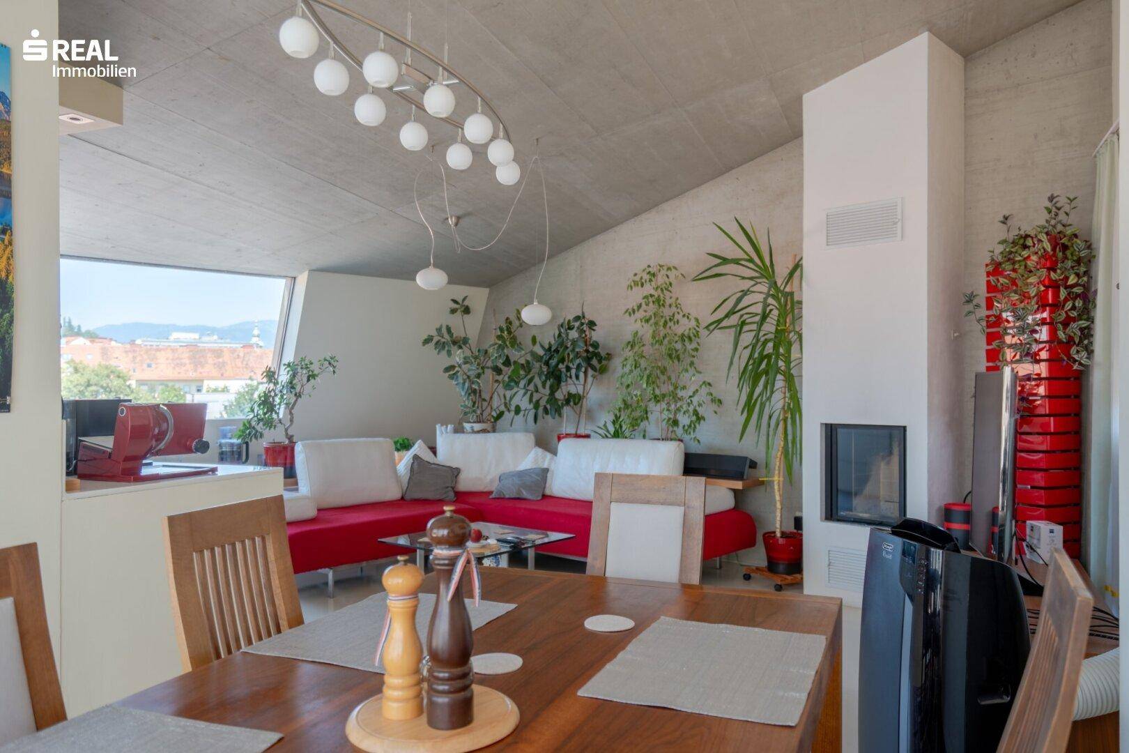 Heller Wohn- und Essbereich mit Kamin, roten Sofas und Blick auf die Stadt.