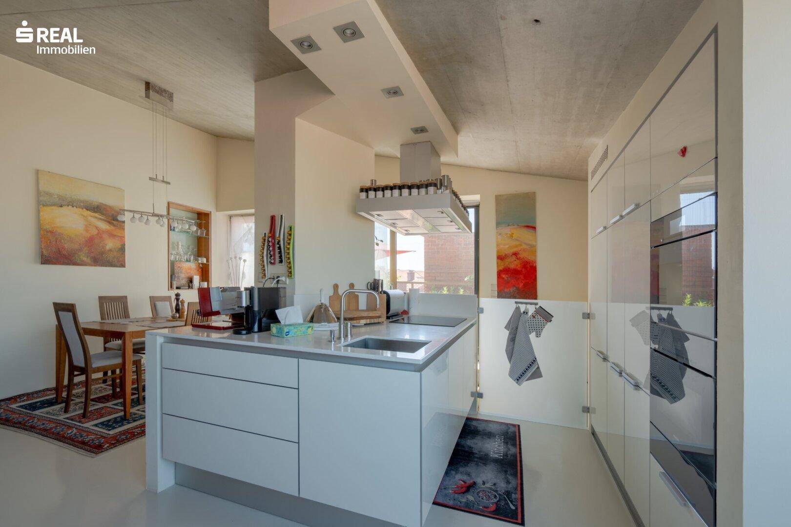 Moderne Einbauküche mit weißen Schränken, Kochinsel und Essbereich im Hintergrund.