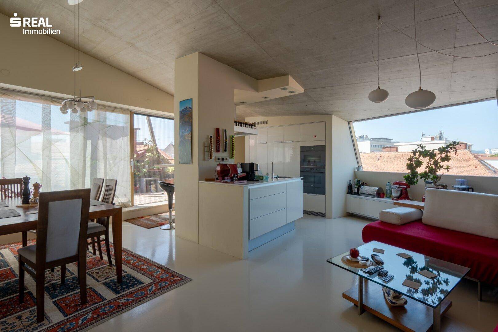 Offener Wohn-Essbereich mit moderner Küche, großen Fenstern und Zugang zur Terrasse.