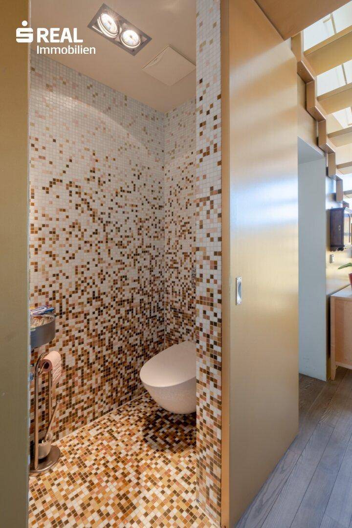 Separate Toilette mit Mosaikfliesen und wandmontiertem WC.