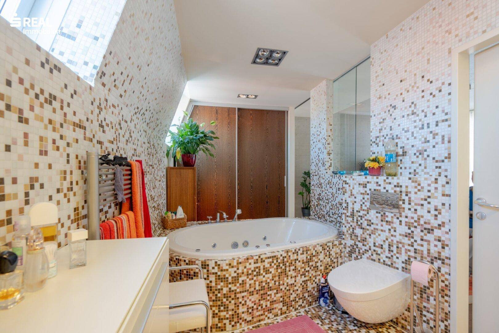 Luxuriöses Badezimmer mit Whirlpool-Badewanne, Mosaikfliesen und wandmontiertem WC.