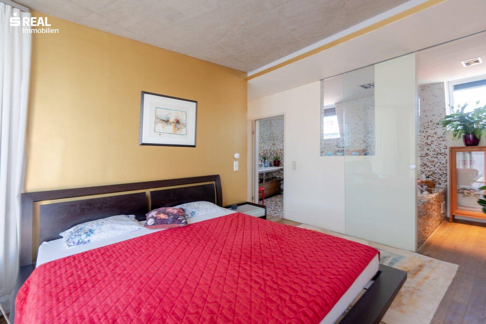 Schlafzimmer mit Doppelbett, goldener Wand und Zugang zum Badezimmer.