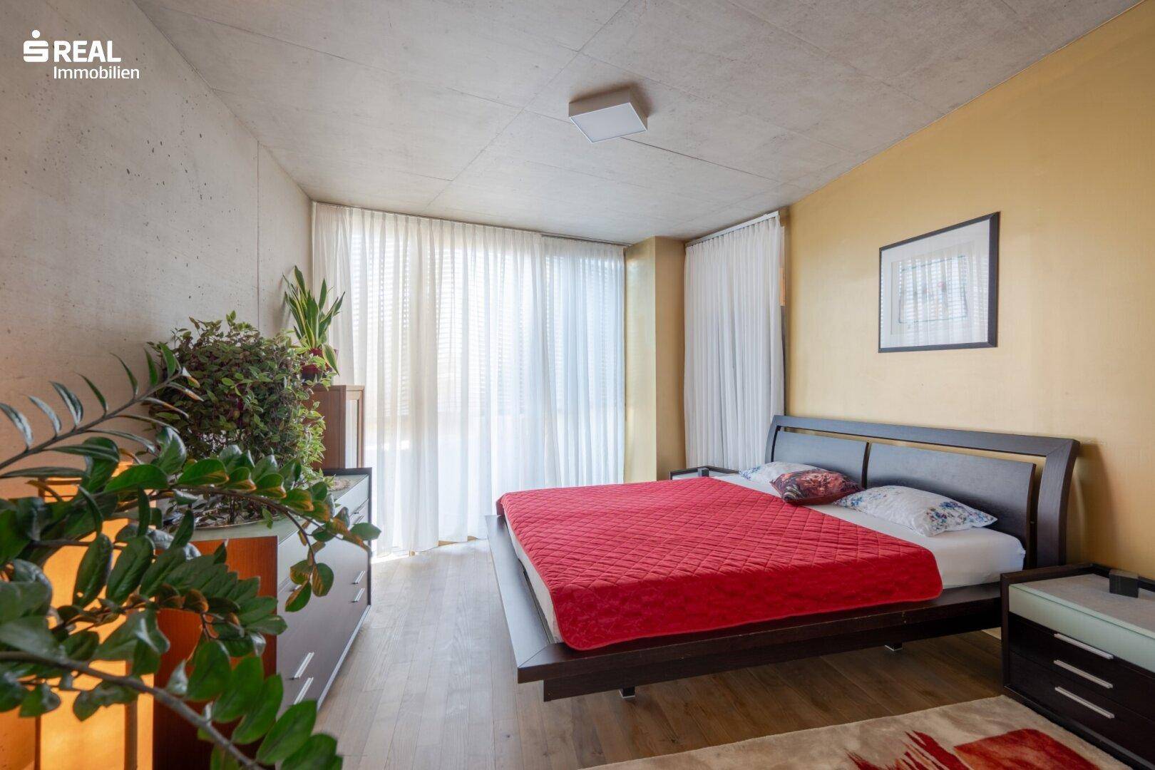 Helles Schlafzimmer mit Doppelbett, großen Fenstern und Blick nach draußen.