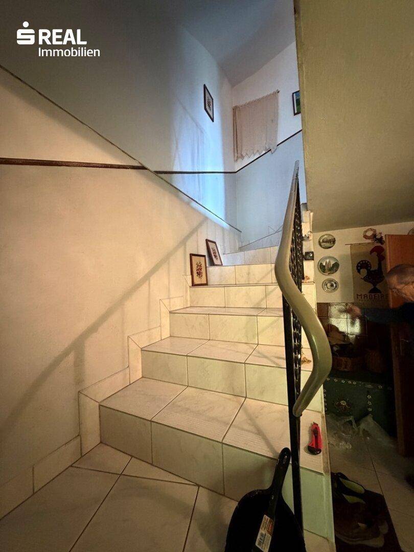 Geflieste Treppe mit schmiedeeisernem Geländer, die in die obere Etage führt.