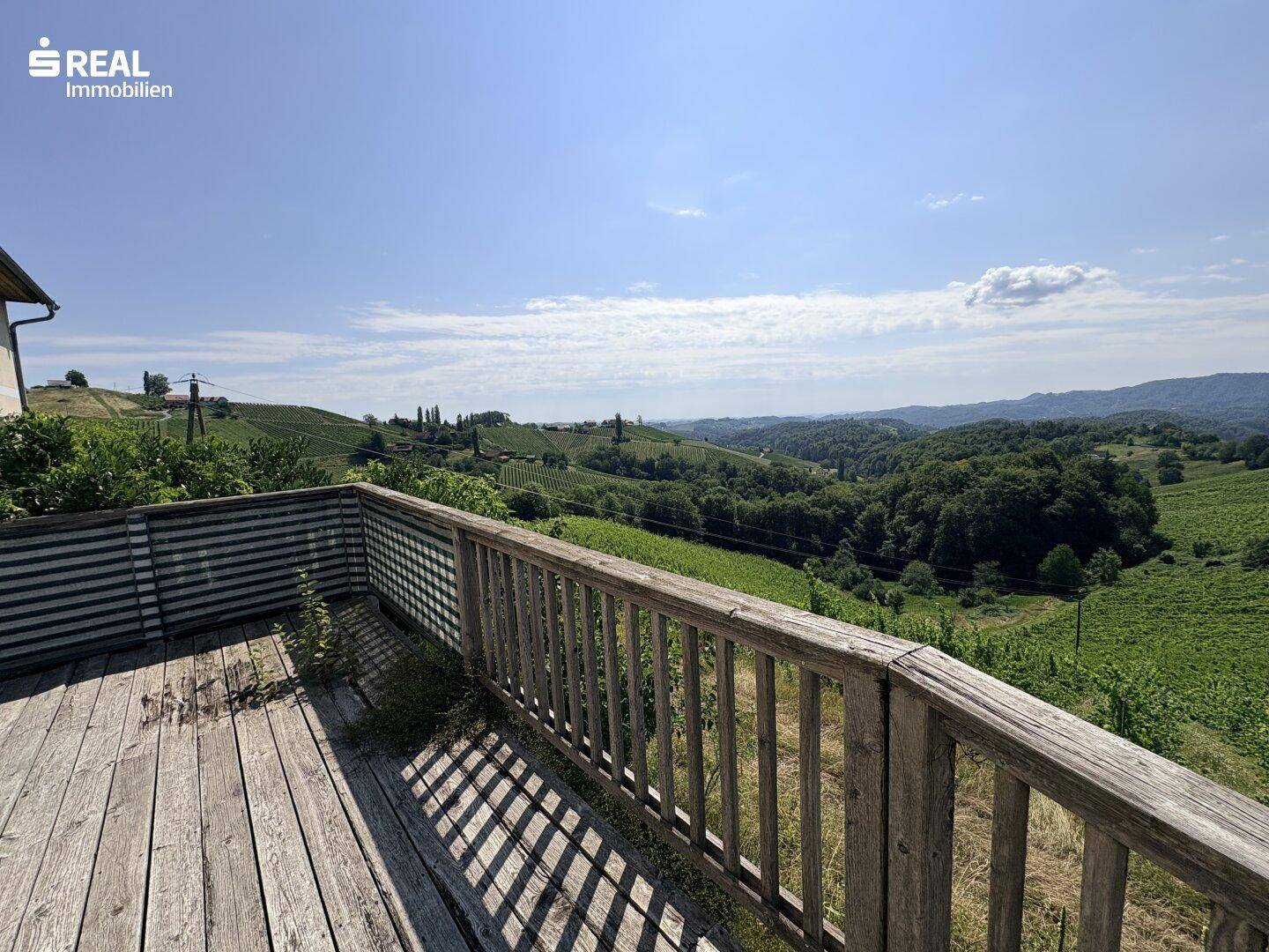 Holzterrasse mit weitem Blick über die umliegenden Weinberge und grüne Hügel unter blauem Himmel.