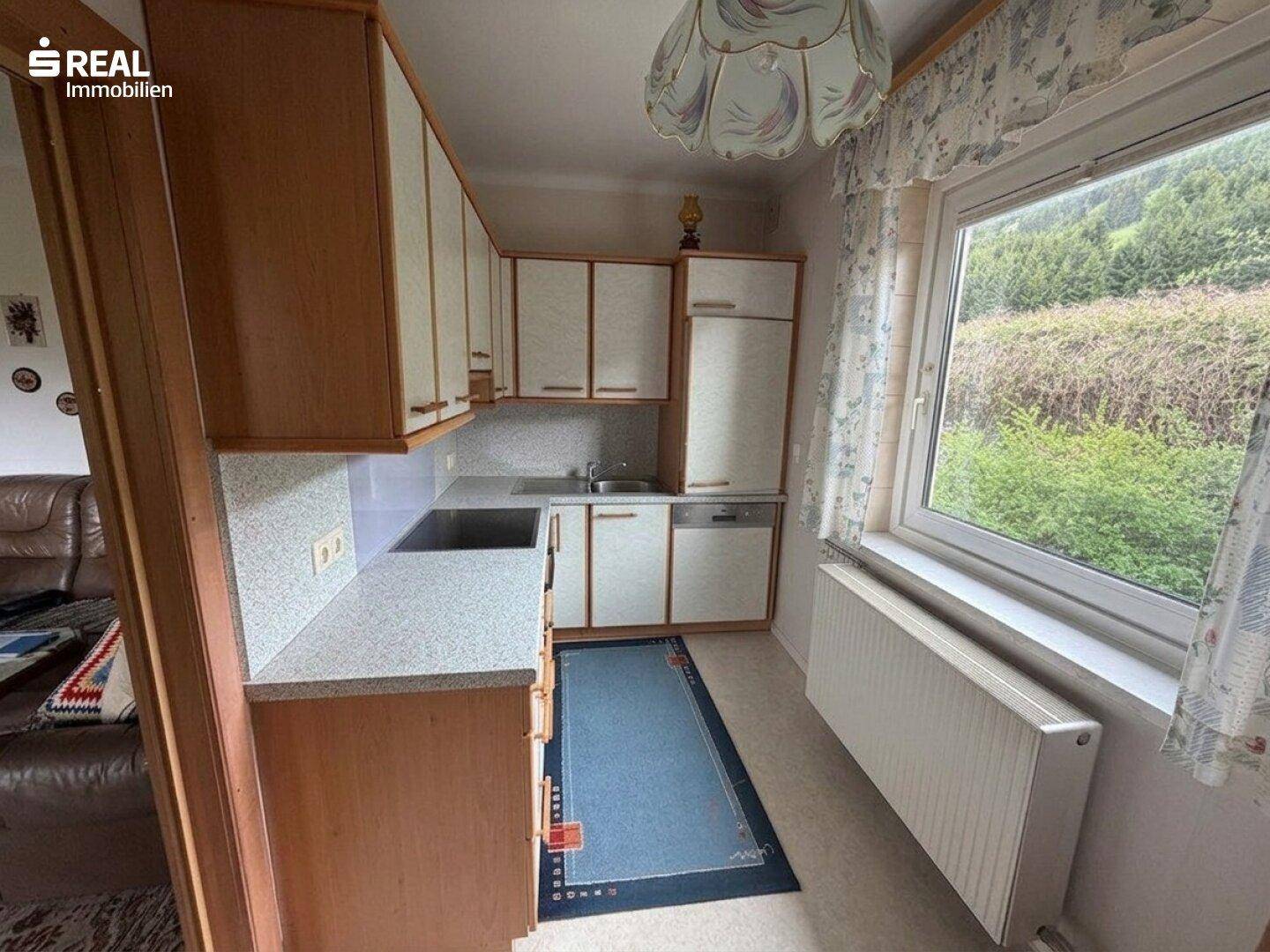 Funktionale Küche mit Einbauschränken, Spüle und Fenster mit Blick auf die Natur.