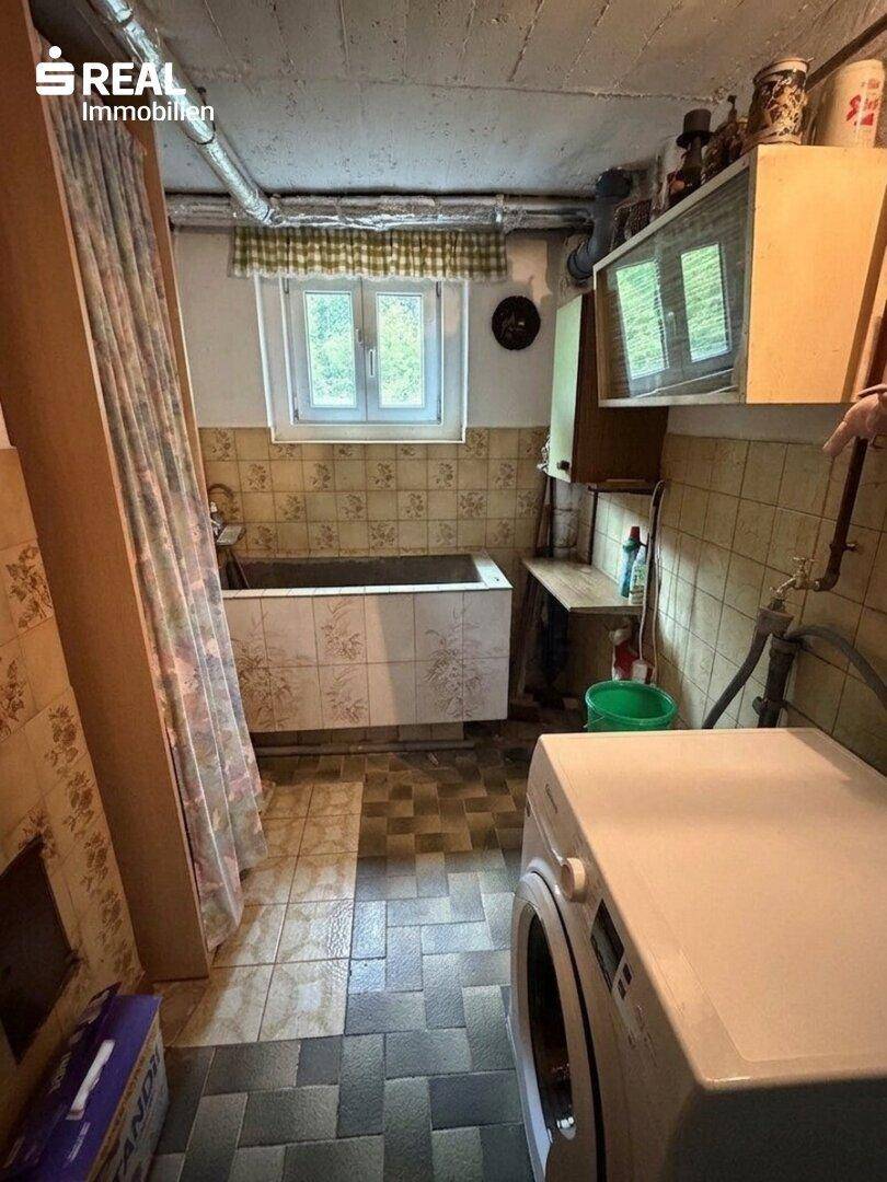 Waschküche im Keller mit Waschmaschine, Badewanne und gefliesten Wänden.