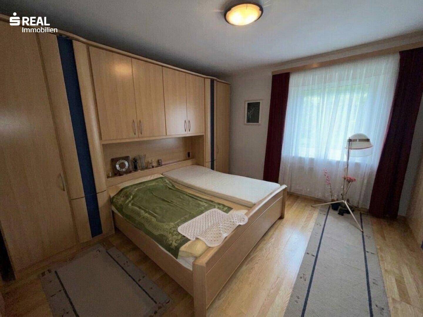 Gemütliches Schlafzimmer mit Holzbett, Einbauschränken und Fenster mit Vorhängen.
